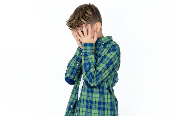 Sad handsome teen boy wearing plaid shirt over white background crying covering her face with her hands. - Photo, Image