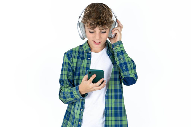 Happy handsome caucasian teenager boy on white studio background feels good while focused in screen of smartphone. People, technology, lifestyle - Photo, Image