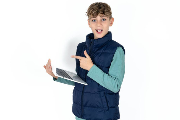 Shocked guapo caucásico adolescente chico en blanco estudio fondo apuntando dedo moderno dispositivo - Foto, Imagen