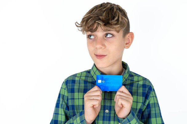 Foto di allegro bel ragazzo caucasico adolescente su sfondo bianco studio tenere carta di debito guardare spazio vuoto - Foto, immagini