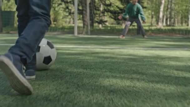 Наземний рівень повільний постріл дитини, що біжить на футбольному полі і стріляє м'ячем під час гри з другом на відкритому повітрі в літній день - Кадри, відео