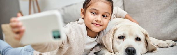 linda chica de edad elemental tomando selfie con perro labrador en casa, animal doméstico y pancarta de niño - Foto, imagen