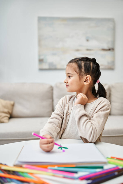 Отвлекающий милый начальный возраст девушка рисунок с цветным карандашом на бумаге в современной квартире - Фото, изображение
