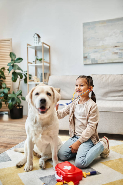šťastný dítě v ležérní oblečení hrát lékař s labrador v moderním obývacím pokoji, hračka stetoskop - Fotografie, Obrázek