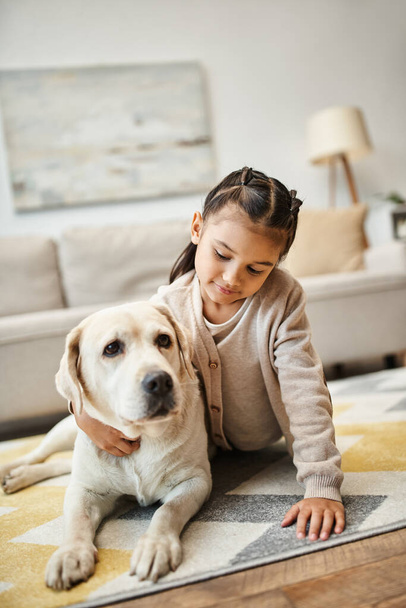 carino bambino in età elementare in abbigliamento casual sdraiato su tappeto con labrador in soggiorno moderno - Foto, immagini