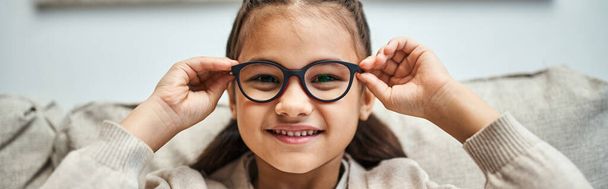 heureuse fille d'âge élémentaire en tenue décontractée portant des lunettes et regardant la caméra, bannière - Photo, image