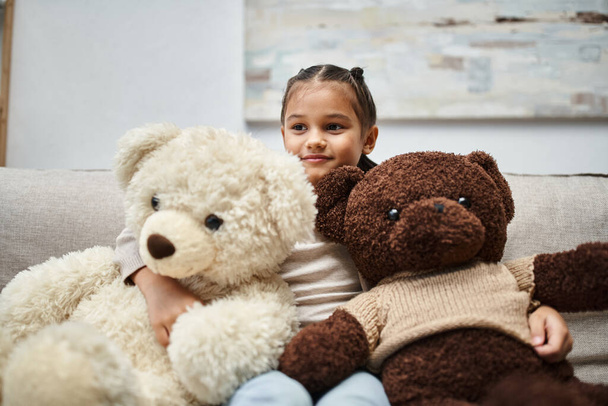 χαριτωμένο παιδί στοιχειώδη ηλικία σε casual φορούν κάθεται σε καναπέ με μαλακό αρκουδάκια στο σαλόνι - Φωτογραφία, εικόνα