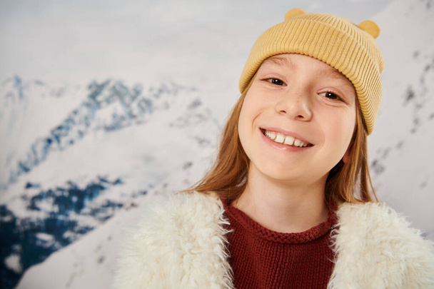 portrait of joyful little cute girl in beanie hat smiling cheerfully at camera, fashion concept - Photo, Image