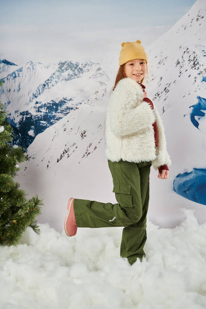 joyful little girl in stylish outfit with one leg raised and smiling at camera, fashion and style - Photo, Image