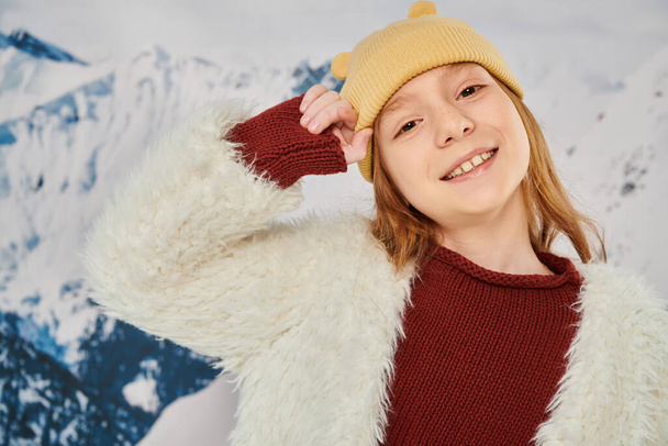 retrato de niña alegre en gorro sombrero con la mano cerca de la cabeza sonriendo alegremente a la cámara, la moda - Foto, imagen