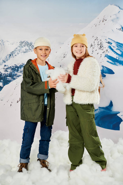 vertical shot of happy preadolescent friends in warm outfits posing with snow in hands, fashion - Photo, Image