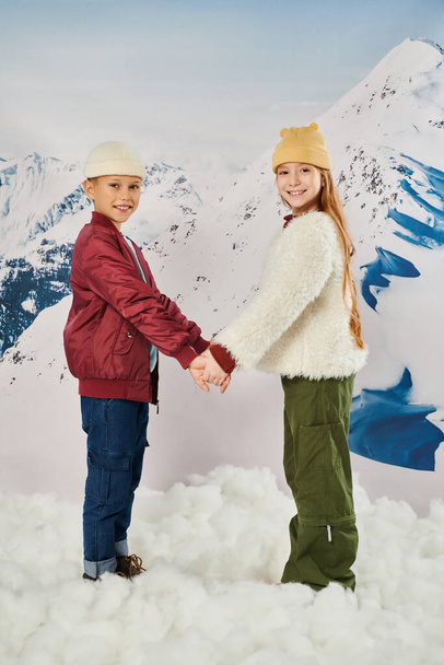 cute preteen friends in stylish winter jackets and beanie hats holding hands and smiling at camera - Photo, Image