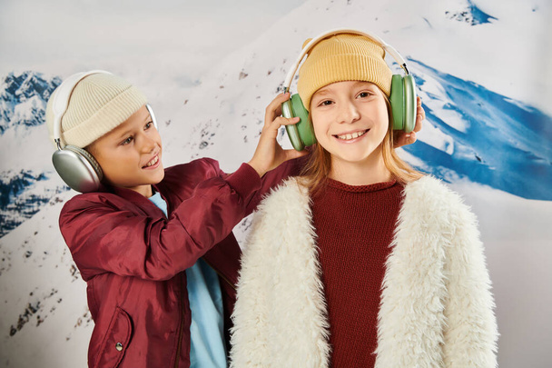 niños preadolescentes alegres en cálidos trajes de moda con auriculares con telón de fondo de montaña, moda - Foto, imagen