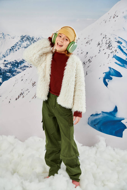kleines Mädchen in stylischer Winterkleidung mit Kopfhörern, Musik hörend und fröhlich lächelnd, Mode - Foto, Bild