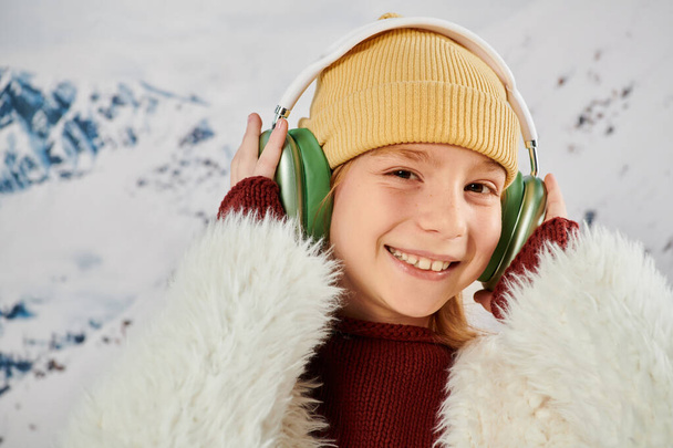 πορτρέτο του χαρούμενου μικρού κοριτσιού αγγίζοντας τα ακουστικά της και χαμογελώντας χαρούμενα στην κάμερα, έννοια της μόδας - Φωτογραφία, εικόνα