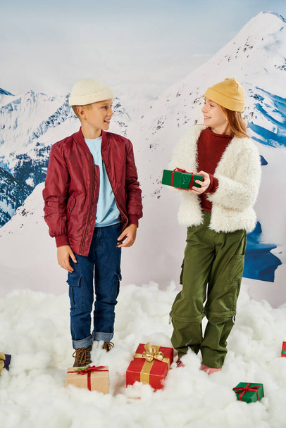 Kleines Mädchen hält Geschenk in der Hand und lächelt ihren Freund mit Berg auf dem Hintergrund an, Modekonzept - Foto, Bild