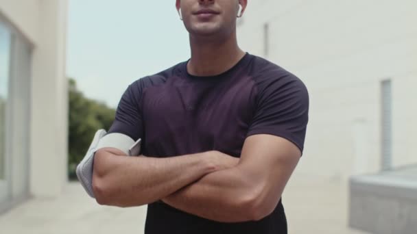 Porträt eines jungen männlichen Sportlers, der Kopfhörer trägt und nach dem Training im Freien in die Kamera schaut - Filmmaterial, Video