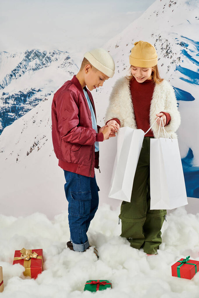 vertical shot of cheerful little friends in stylish winter attires looking happily in present bag - Photo, Image