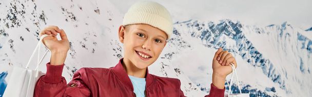 preteen αγόρι σε κομψά ρούχα κρατώντας τις παρούσες τσάντες και χαμογελώντας στην κάμερα, έννοια της μόδας, πανό - Φωτογραφία, εικόνα