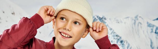 jolly μικρό αγόρι σε κομψή ενδυμασία βάζοντας το μοντέρνο καπέλο του beanie, έννοια της μόδας, πανό - Φωτογραφία, εικόνα