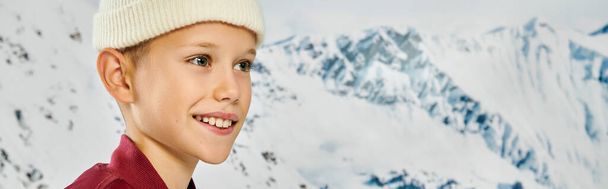 malý roztomilý chlapec v čepici odvrací pohled se zasněžené hory na pozadí, módní koncept, banner - Fotografie, Obrázek