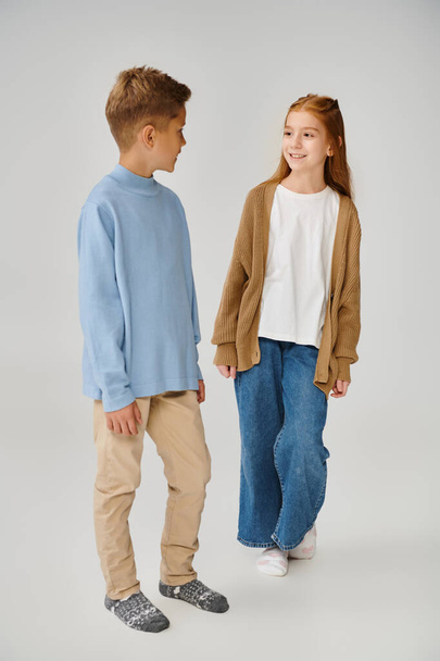 vrolijk klein meisje in gebreide vest glimlachend naar tiener jongen in blauwe sweater, mode concept - Foto, afbeelding