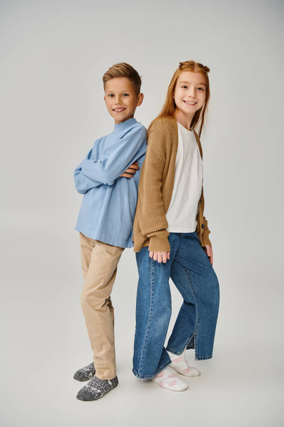 vertical shot of jolly preteen friends in casual warm outfits posing back to back on gray backdrop - Photo, Image