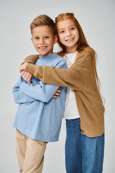 вертикальный снимок веселых маленьких друзей в стильных нарядах, обнимающих и улыбающихся в камеру, мода - Фото, изображение