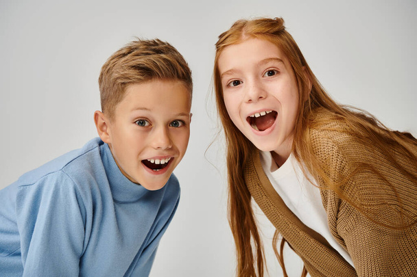 portret van vrolijke kleine vrienden die verbazingwekkend naar de camera kijken op een grijze achtergrond, modeconcept - Foto, afbeelding