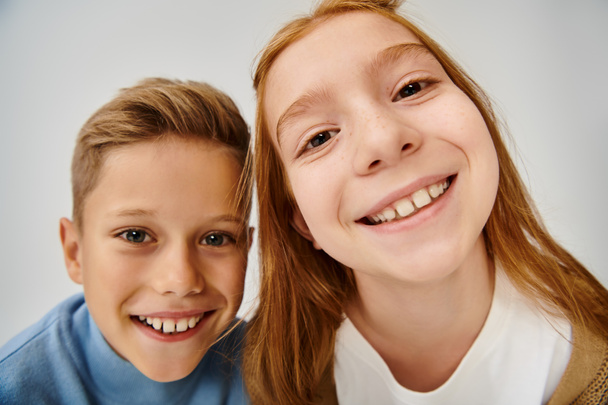 primer plano de dos niños preadolescentes alegres sonriendo a la cámara en el fondo gris, concepto de moda - Foto, Imagen