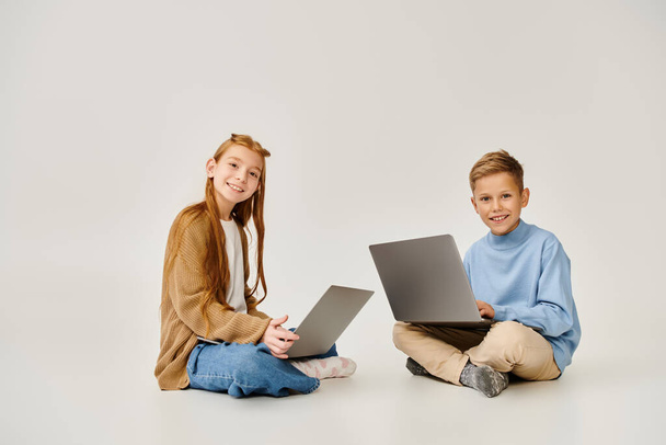 jolly little children in stylish attires on floor with laptops smiling at camera, fashion concept - Photo, Image