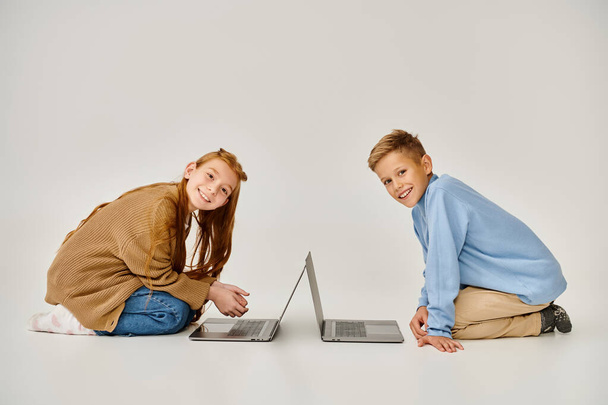 Веселые друзья-подростки в зимней одежде на полу с ноутбуками, улыбающимися в камеру, концепция моды - Фото, изображение