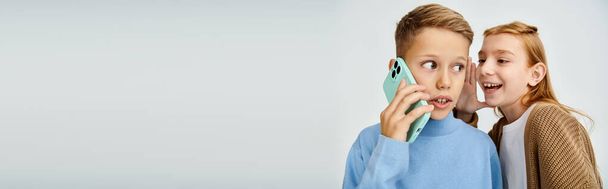 geschokt tiener jongen praten per telefoon terwijl zijn vrolijke peer fluistert iets in zijn oor, banner - Foto, afbeelding