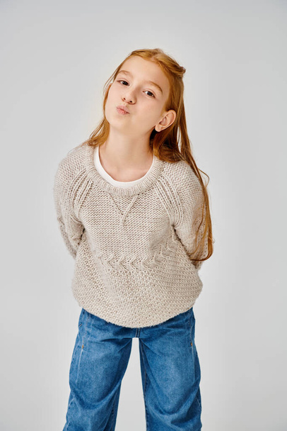 jolly preadolescent girl in knitted trendy sweater looking at camera with pouted lips, fashion - Photo, Image