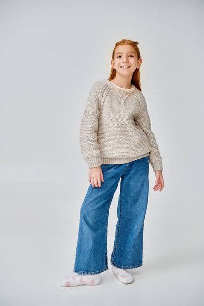 мила дівчина-підліток в зимовому стильному вбранні позує на сірому фоні, посміхаючись на камеру, мода - Фото, зображення