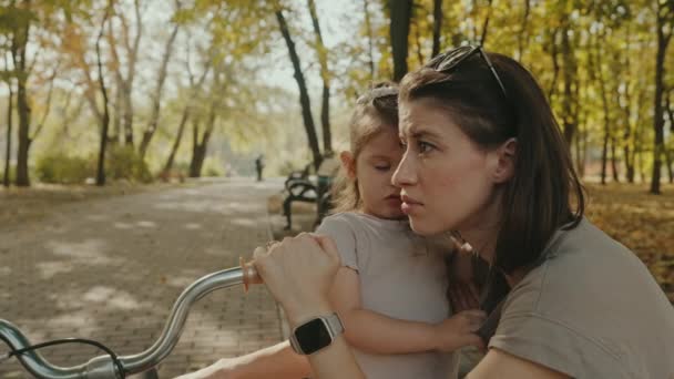 Madre e hija de pie abrazadas juntas en el parque, después de una dura lección de montar en bicicleta. Naturaleza de verano al aire libre. Mamá abrazando niño. - Imágenes, Vídeo