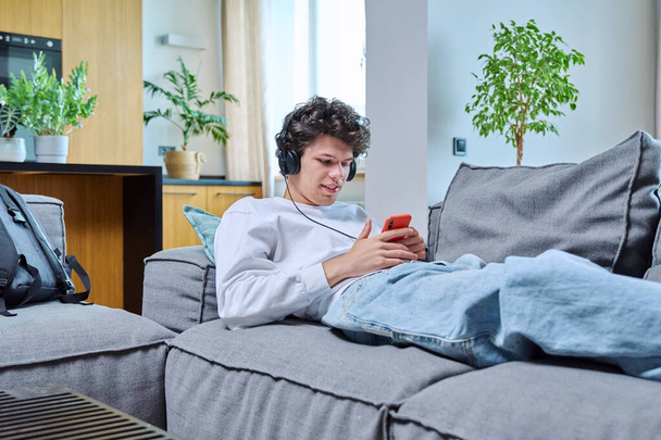 Young guy having video call chat conference lying on sofa at home using smartphone. Male recording video blog making online broadcast talking with friends study work lifestyle mobile applications - Photo, image