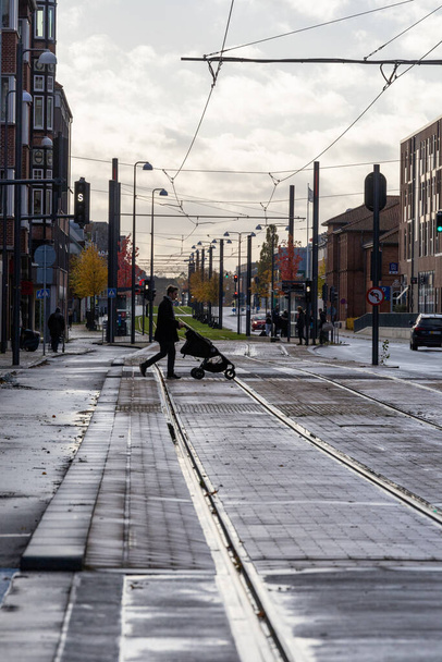 Odense, Dania 30 paź 2023 Mężczyzna popycha wózek przez tory tramwajowe w centrum na Ostre Stationsvej. - Zdjęcie, obraz