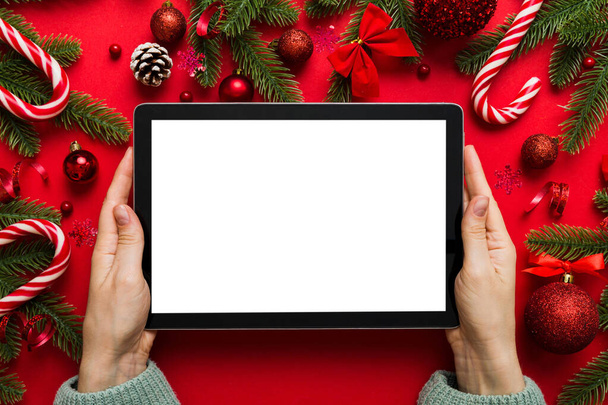 Boże Narodzenie zakupy online z domu, ręce kobiet trzymając tablet z pustym białym wyświetlaczem widok z góry. kobieta ręka gospodarstwa tabletki z pustym ekranem, choinka i prezenty na tle. - Zdjęcie, obraz
