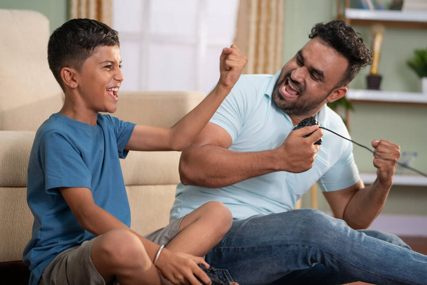Focus on kid, cheerful indian father and son celebrating win while playing video game by using joystick at home - concept of Joyful gaming, family Fun and weekend activities - Photo, Image