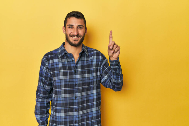 Молодий іспаномовний чоловік на жовтому тлі, що показує номер один з пальцем. - Фото, зображення