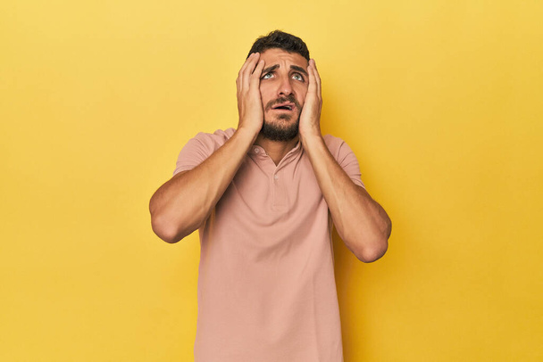 Junger hispanischer Mann auf gelbem Hintergrund jammert und weint untröstlich. - Foto, Bild