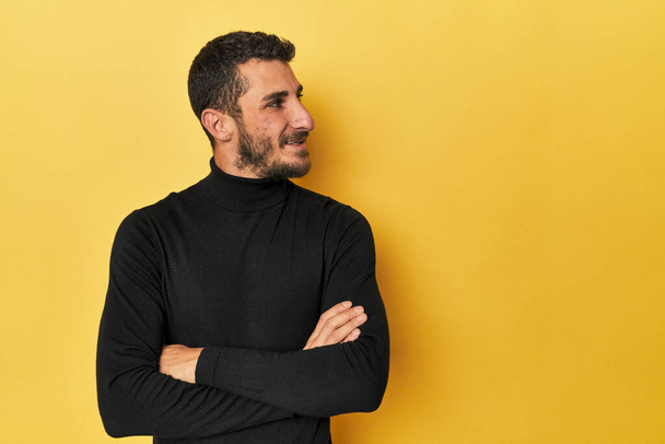 Fiatal spanyol férfi sárga háttérrel mosolygós magabiztos keresztbe tett karokkal. - Fotó, kép