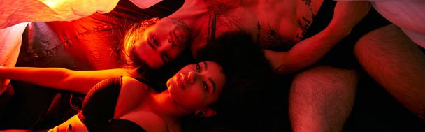 attractive diverse couple lying sensually together under bedsheet surrounded by lights, banner - Photo, Image