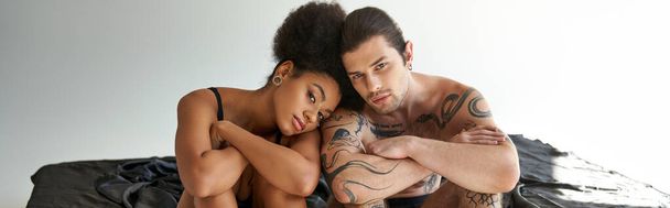 appealing young multiracial couple in underwear sitting close to each other on bed, banner - Photo, Image