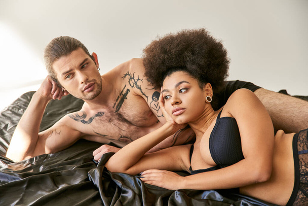 若い多文化魅力的なカップルは一緒にベッドに横たわり,離れて見ている - 写真・画像