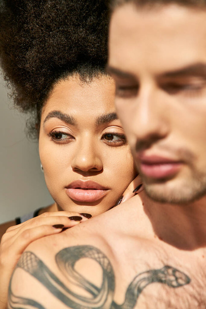 joven con tatuajes abrazando amorosamente a su atractiva novia afroamericana sobre fondo gris - Foto, imagen