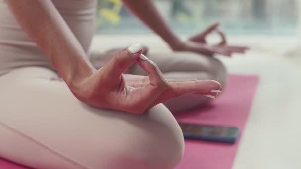 Primer plano de las manos de la mujer sentada en posición de loto mientras está sentada en la esterilla con temporizador en el teléfono inteligente, meditación - Metraje, vídeo