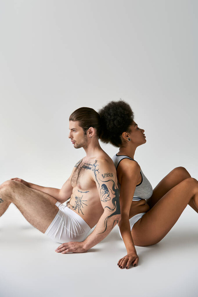 привлекательный молодой разнообразный парень и девушка сидя спиной к спине на полу, сексуальная пара - Фото, изображение