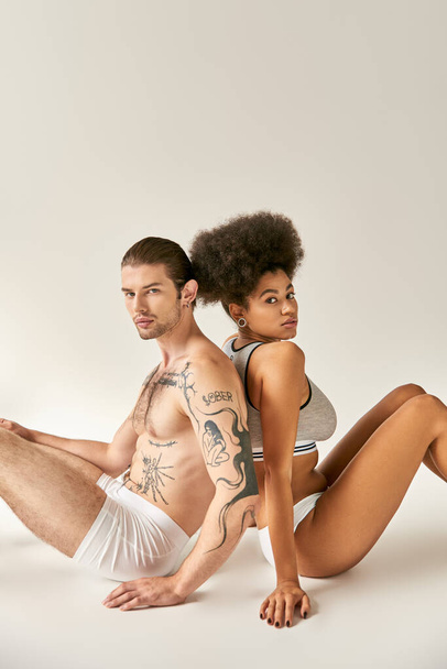 attractive multicultural boyfriend and girlfriend sitting back to back on floor, sexy couple - Foto, Imagem